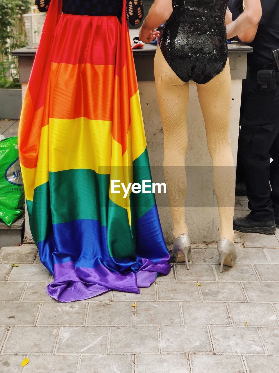 Low section rear view of lesbians standing on street with rainbow flag