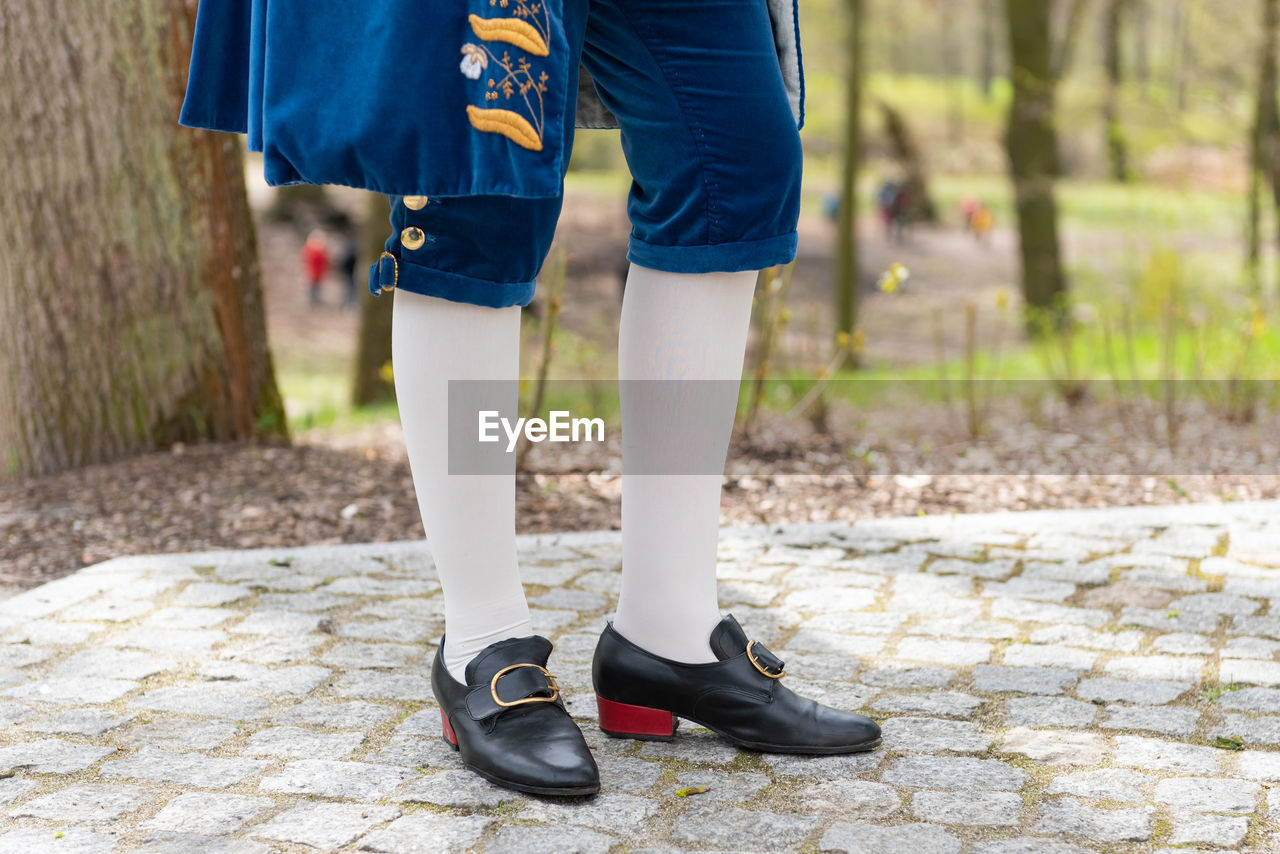 Details of a man's dress in a baroque costume. white stockings and black shoes, golden buttons.