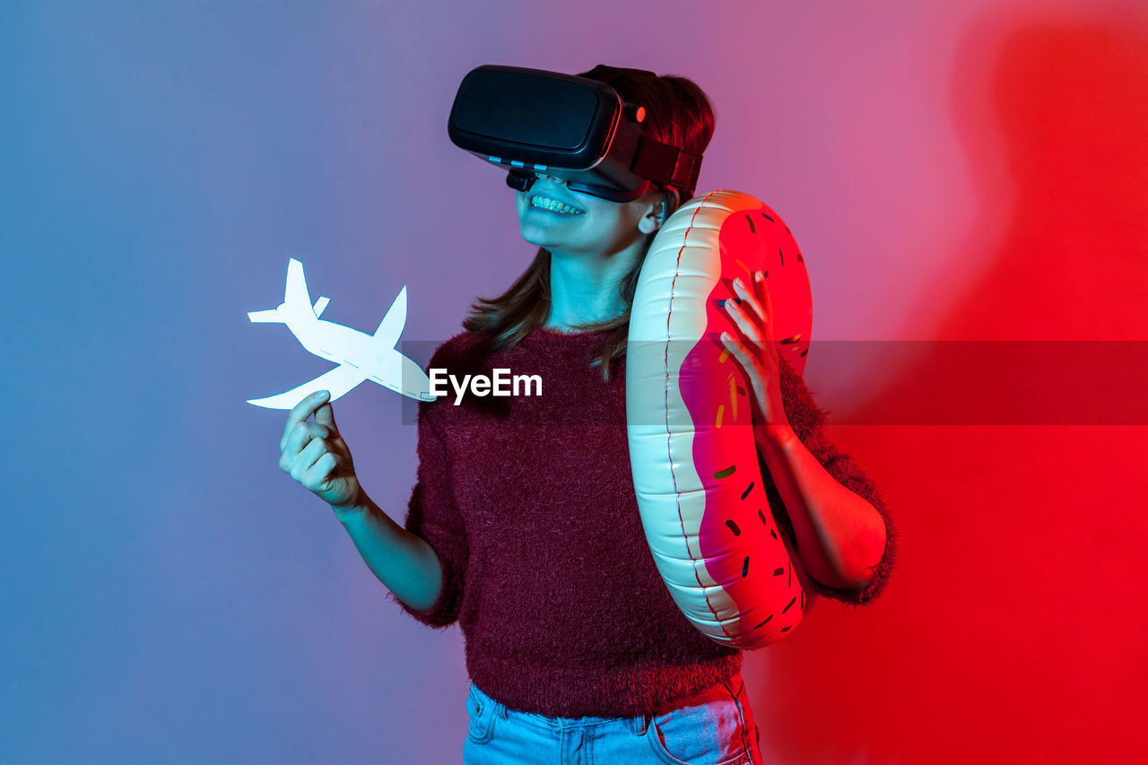 Woman wearing virtual reality simulator while standing against colored background