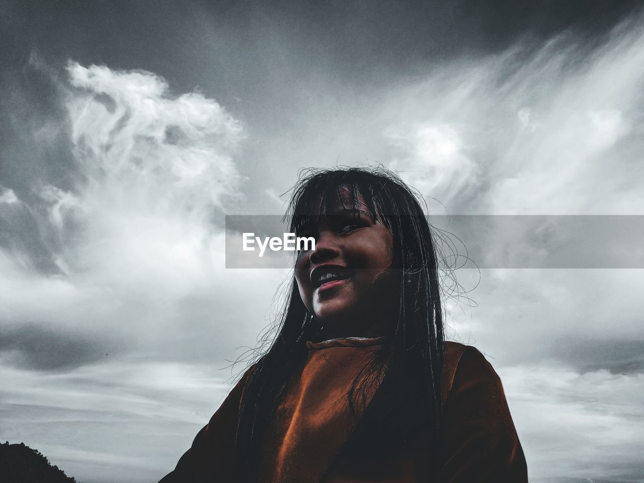 LOW ANGLE PORTRAIT OF YOUNG WOMAN LOOKING AT SKY