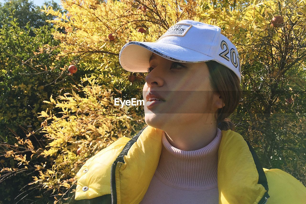 yellow, one person, autumn, spring, plant, headshot, leisure activity, nature, portrait, lifestyles, day, tree, sunlight, adult, young adult, hat, leaf, women, looking, flower, fashion accessory, outdoors, clothing, looking away, casual clothing, front view, person, green, standing, land, sun hat, growth, cap, fashion, human face, child, female