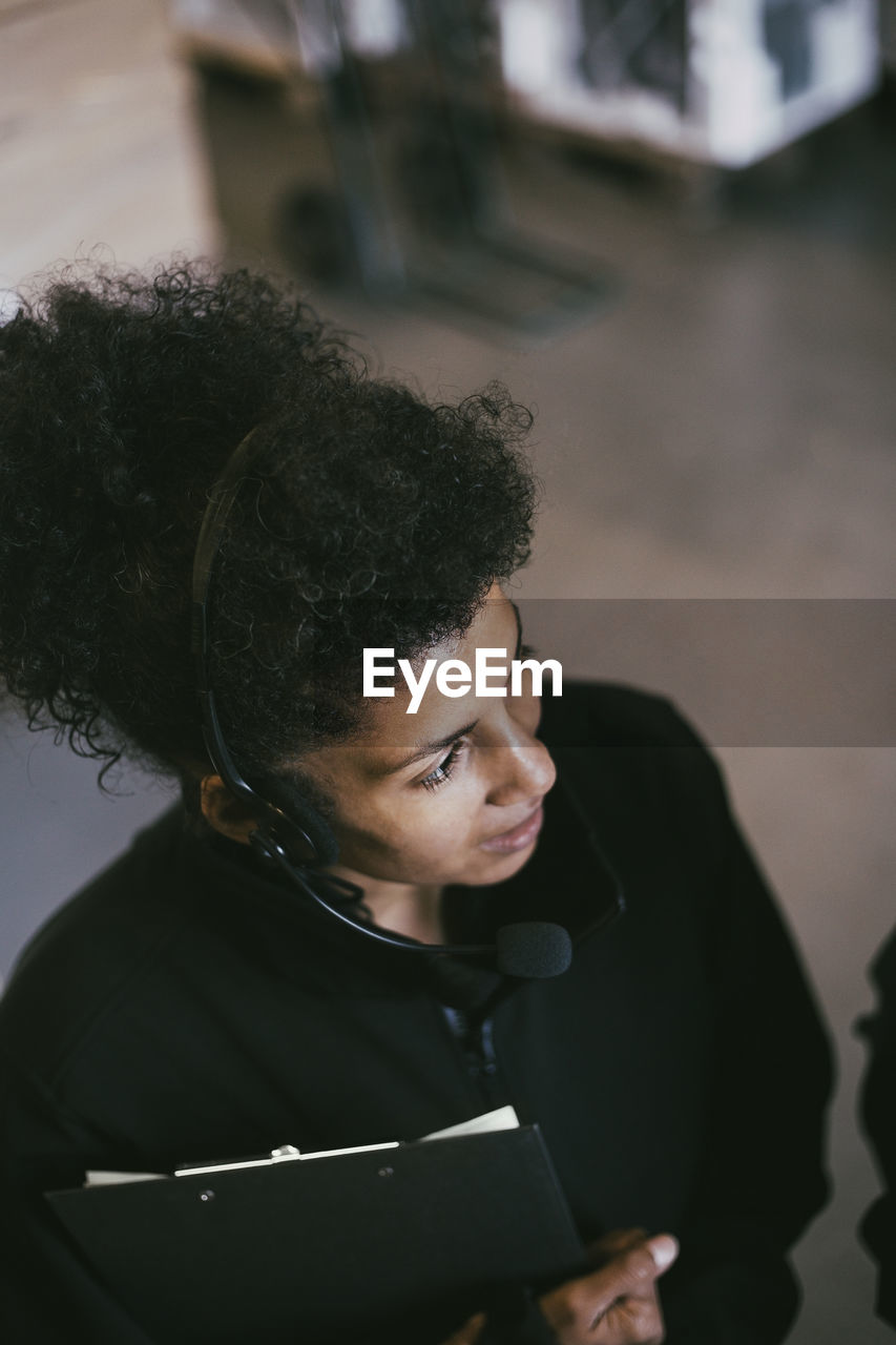 High angle view of female entrepreneur with headset looking away while working in warehouse