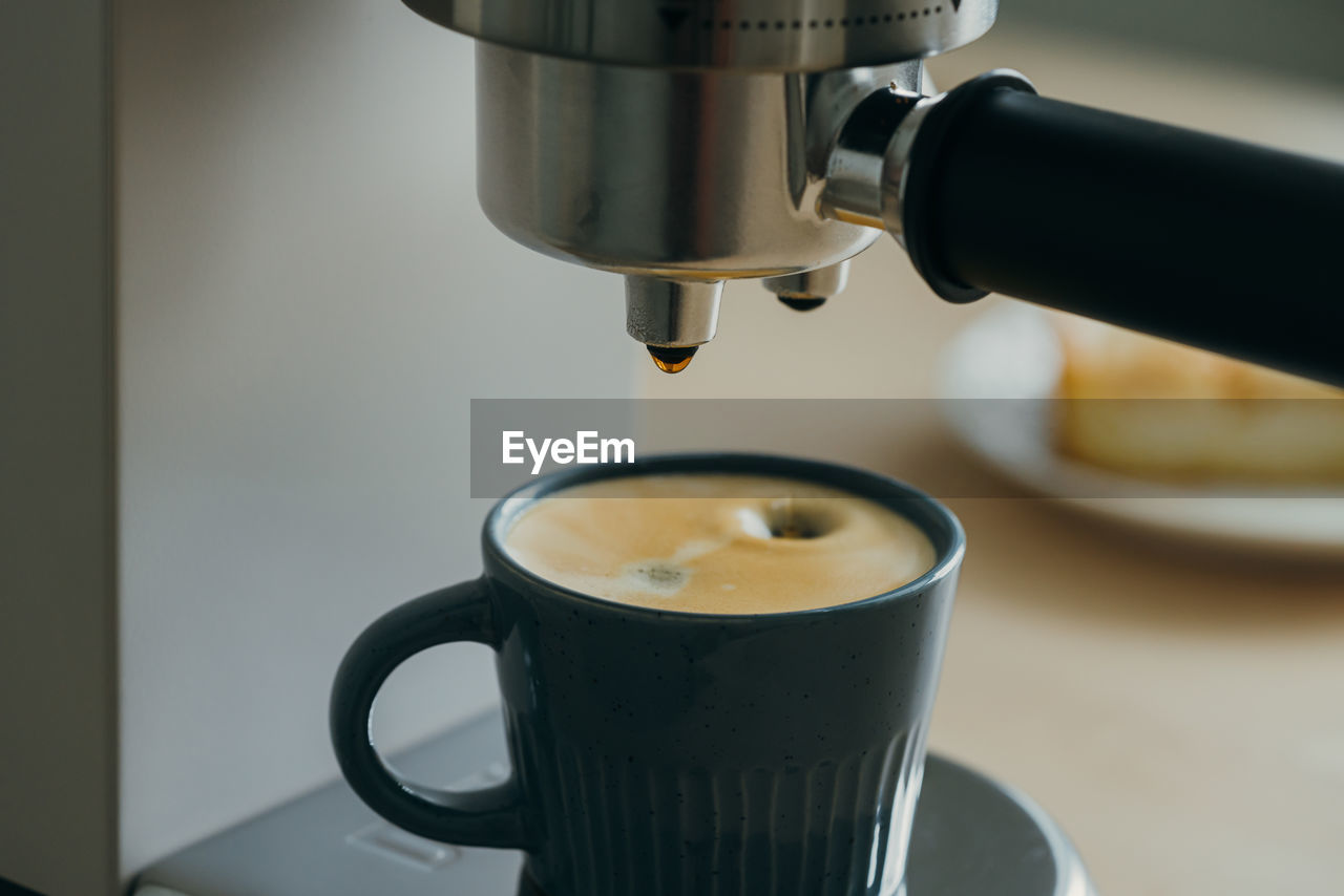 Morning ritual at breakfast with pouring coffee from coffee machine, drops of espresso dripping