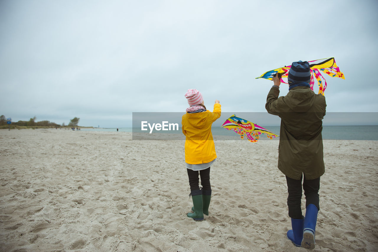 Rear view of boy holding kite standing on beach against sky