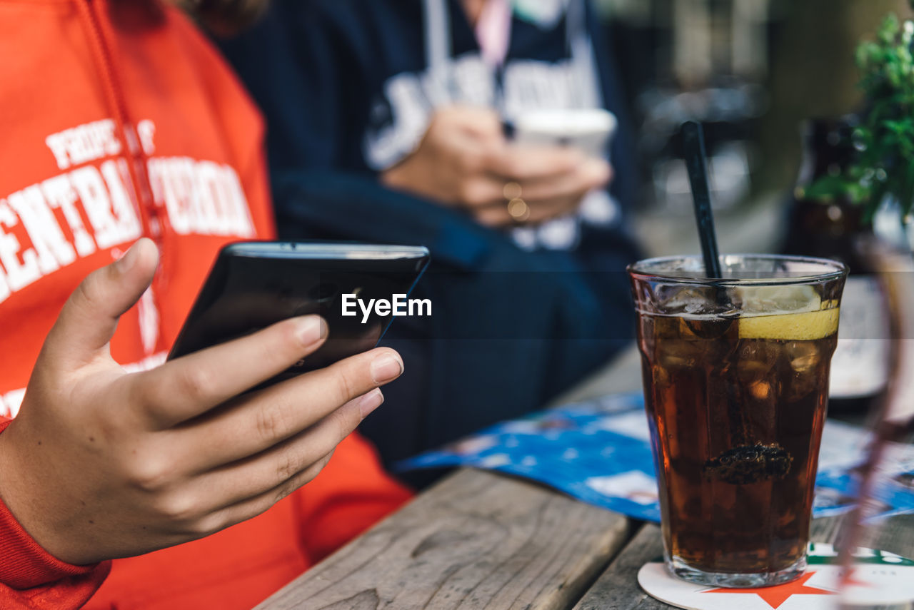 Midsection of woman text messaging on phone while sitting at table