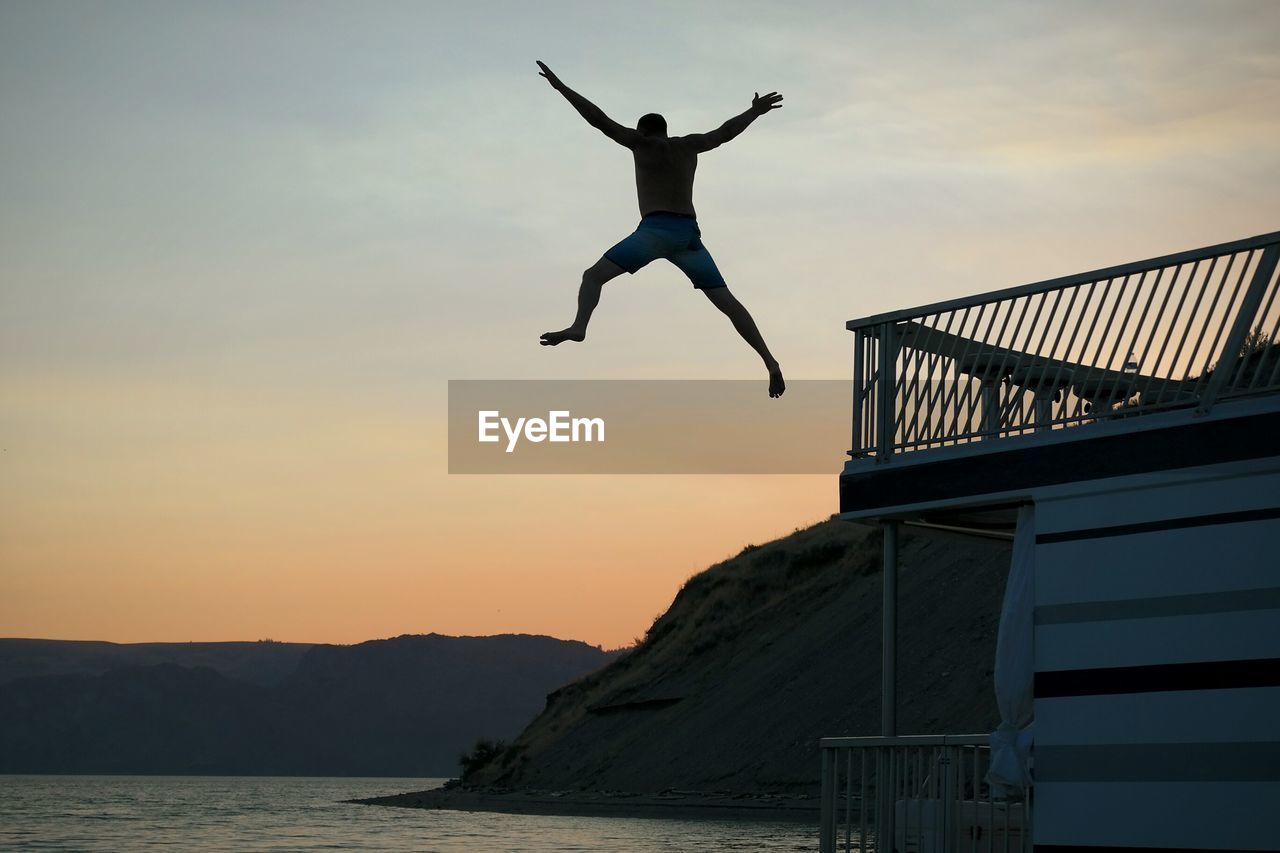 Man jumping in sea against sky during sunset