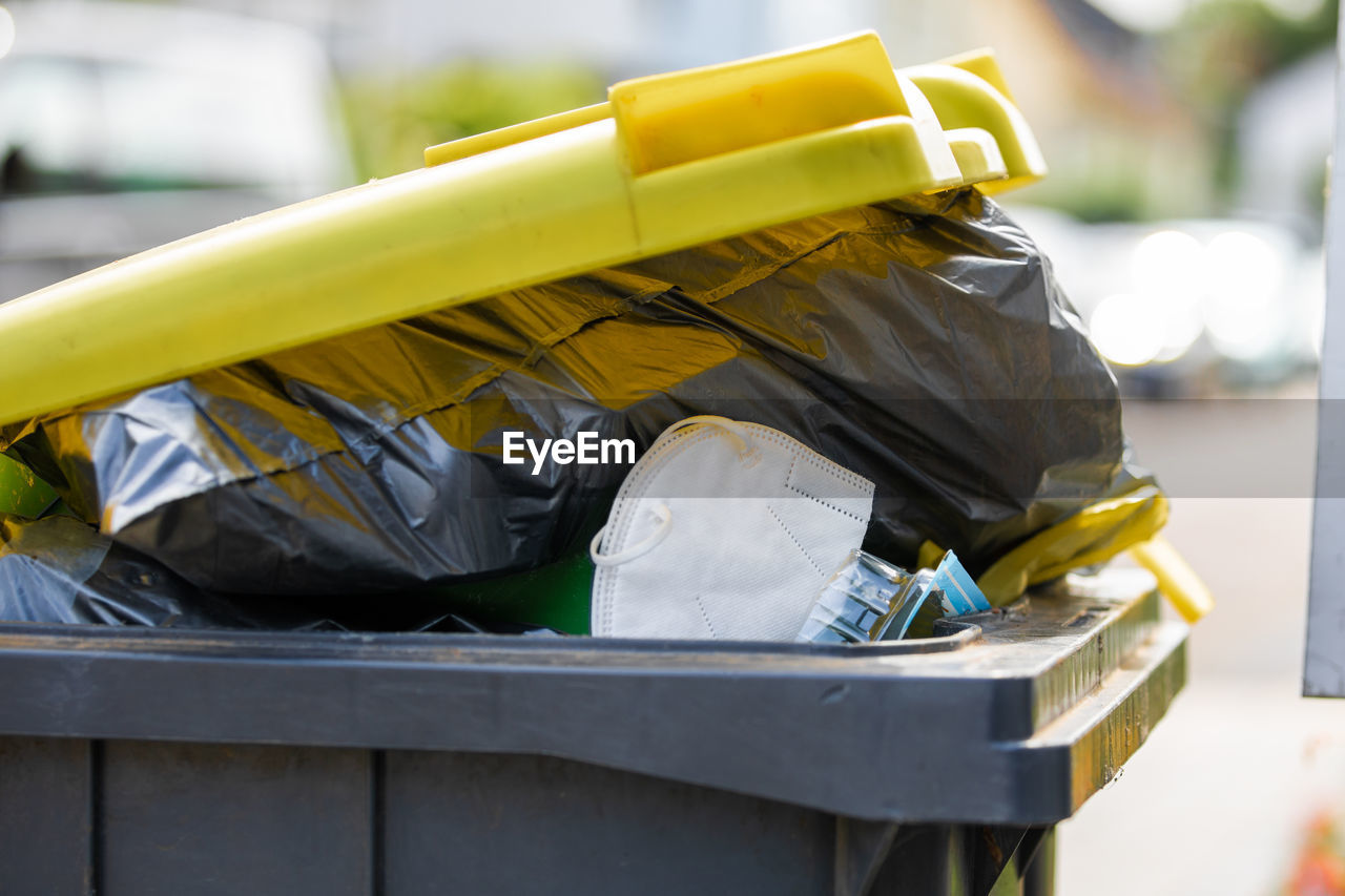 Full garbage trash can with ffp2 face mask standing at sidewalk waiting to get empty