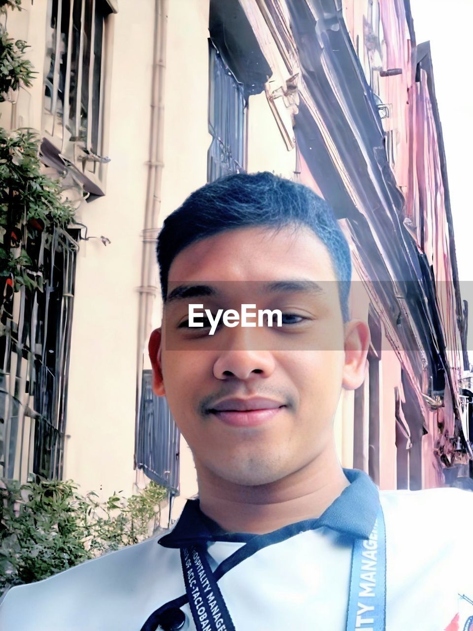 portrait, one person, architecture, looking at camera, headshot, smiling, building exterior, young adult, city, person, happiness, front view, adult, men, built structure, blue, emotion, day, lifestyles, clothing, building, nature, outdoors, spring, human face, cheerful, standing, city life, sunlight, black hair