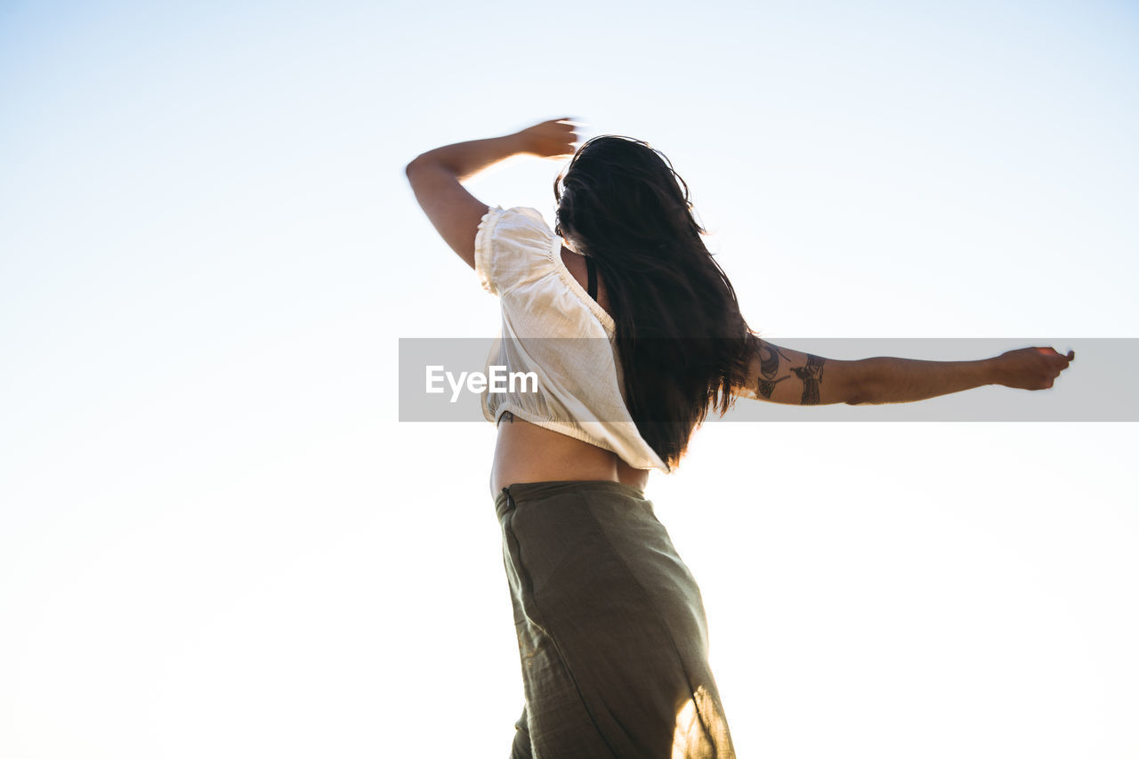 Young latina woman dancing by the ocean at golden hour in summertime
