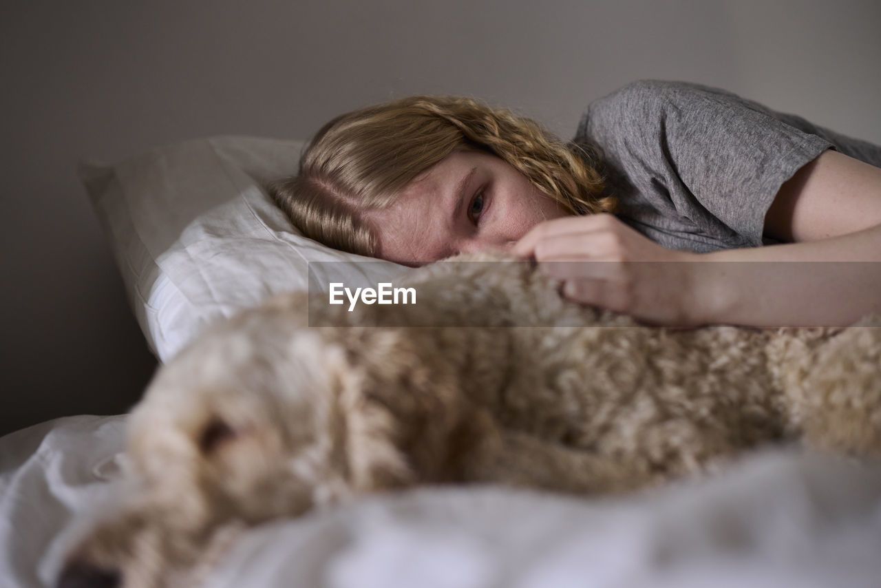 Crying young woman hugging dog in bed