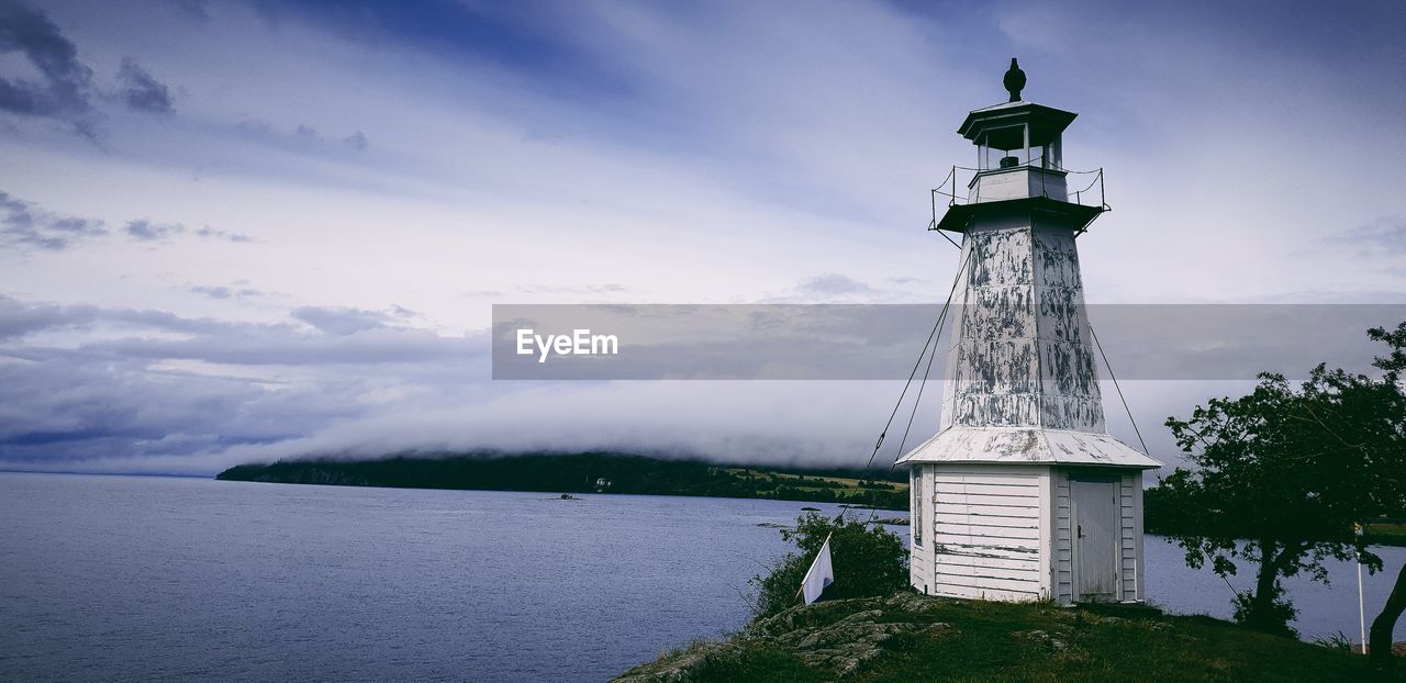 Lighthouse by building against sky