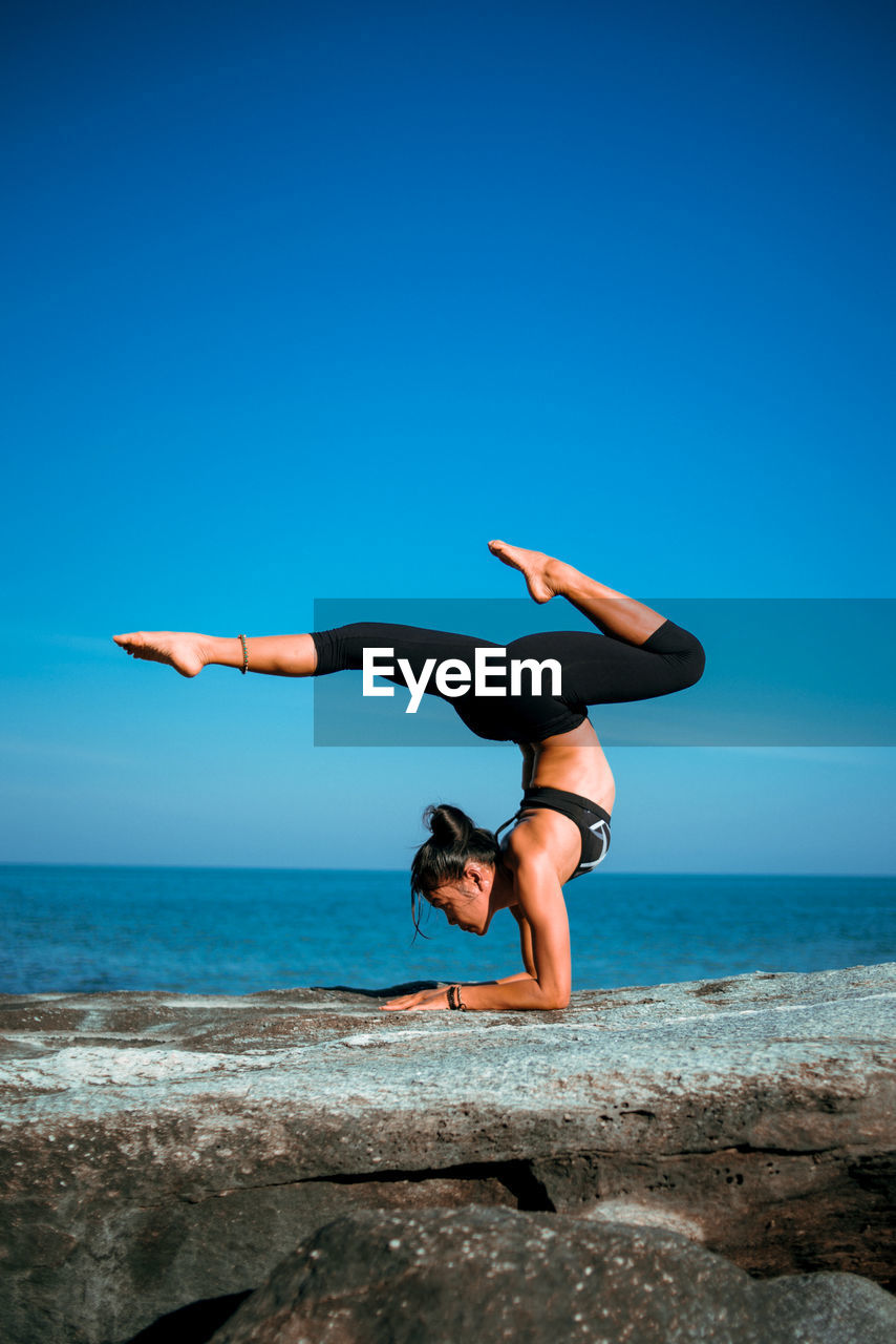 WOMAN JUMPING ON BEACH AGAINST CLEAR SKY