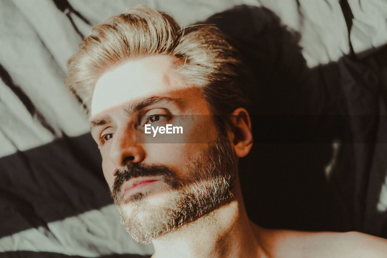 Close-up of thoughtful man lying on bed at home