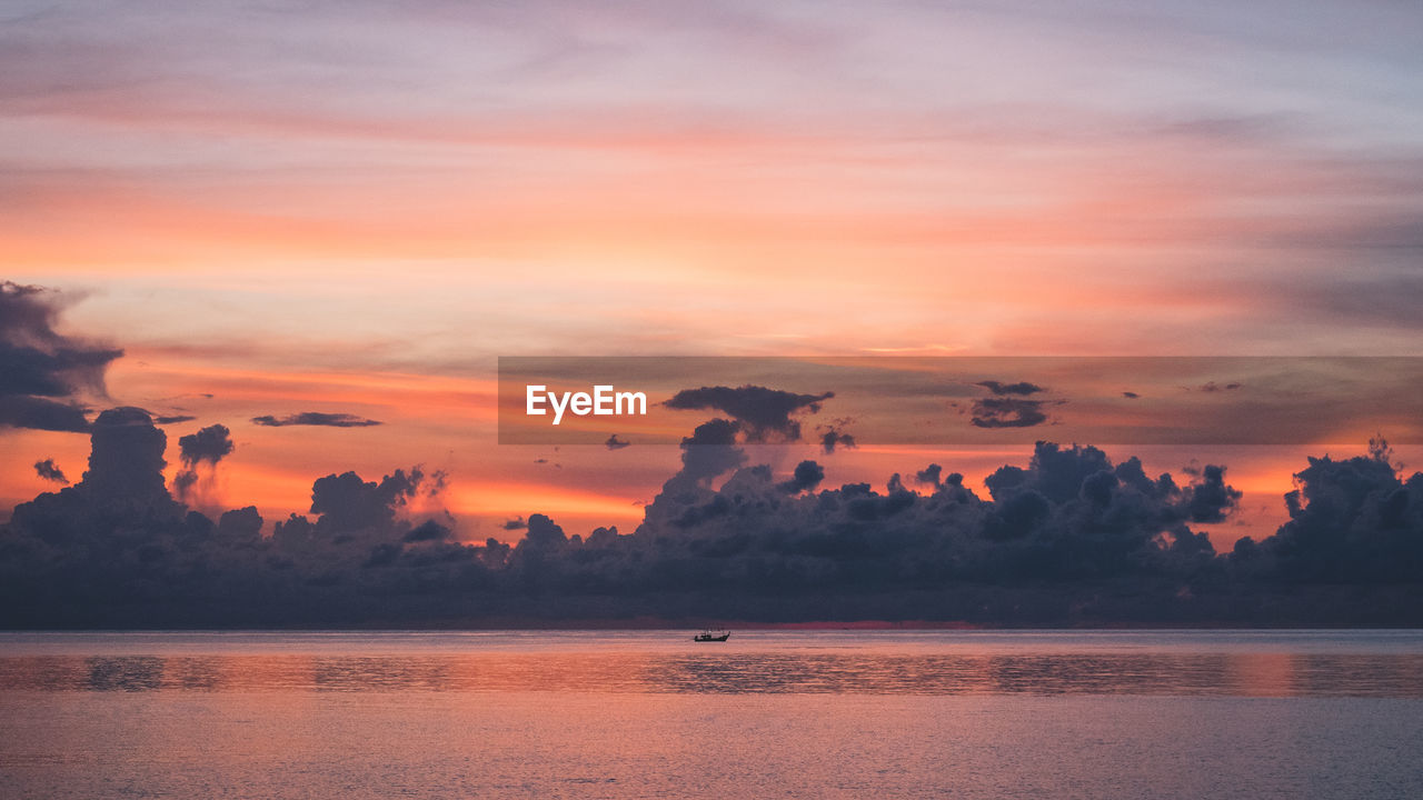 Island's bay dawn with orange sky and lonely boat against dramatic cloud. koh samui, thailand.