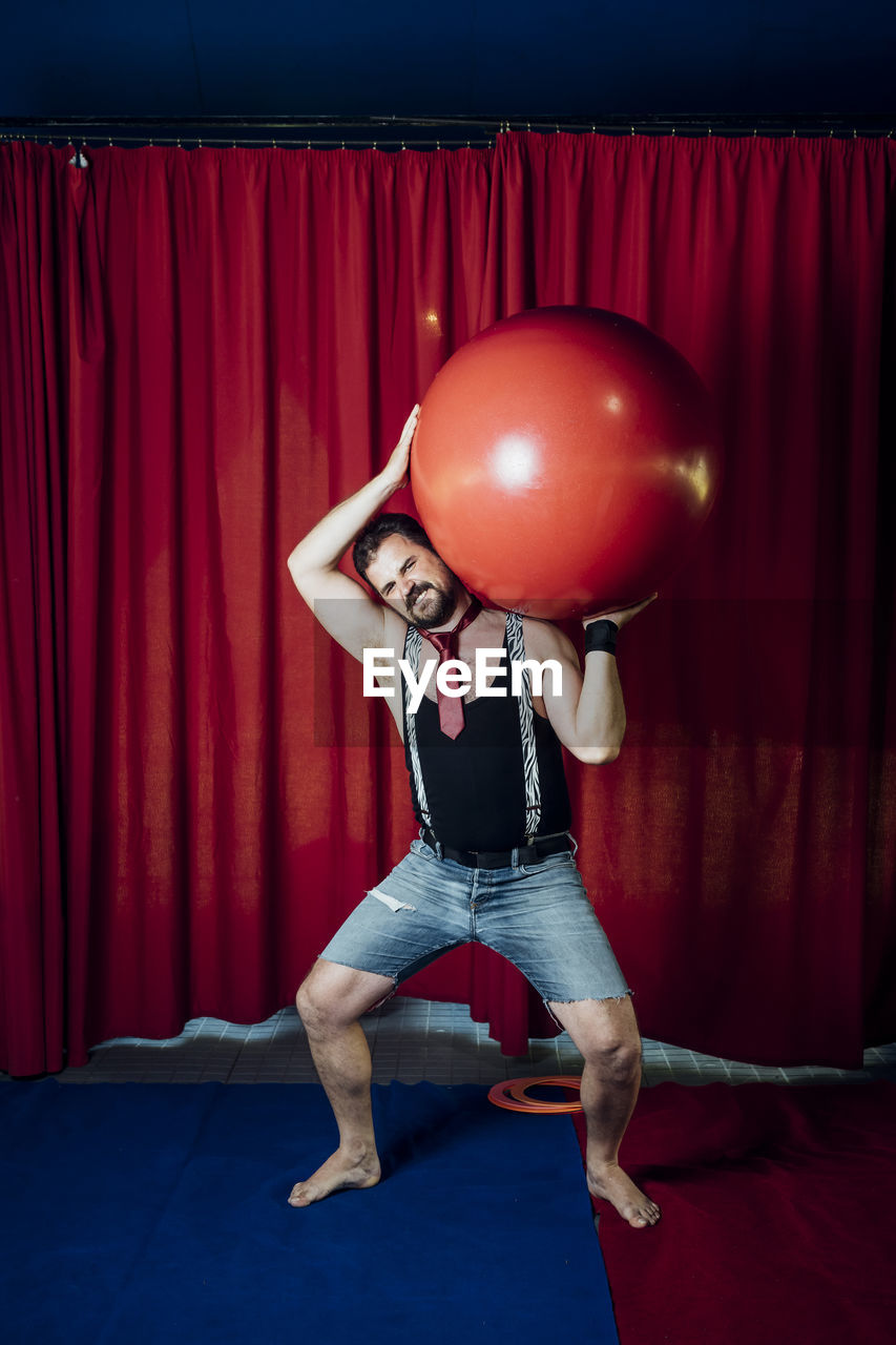 Male circus acrobat carrying red ball while performing on stage