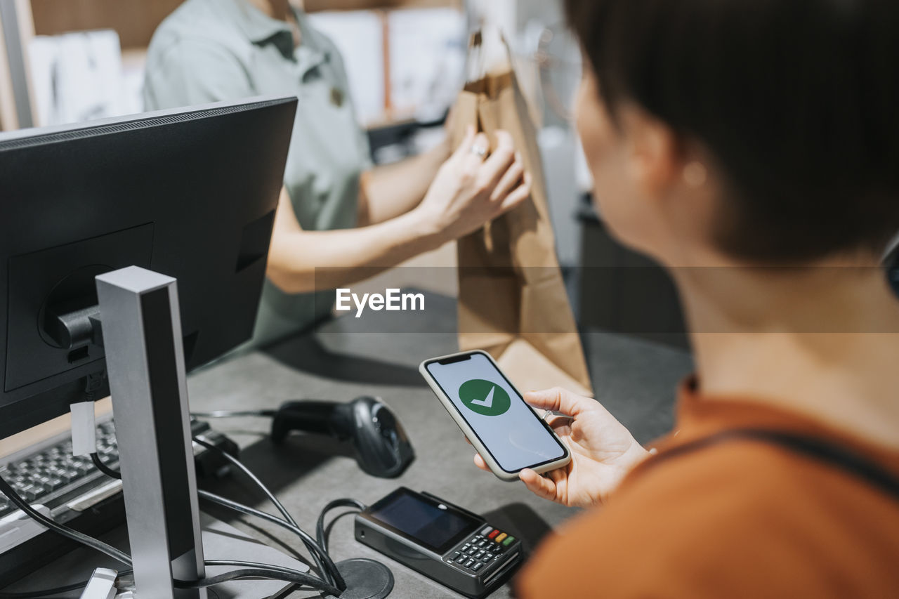 Female customer scanning credit card reader while paying through mobile phone in electronics store