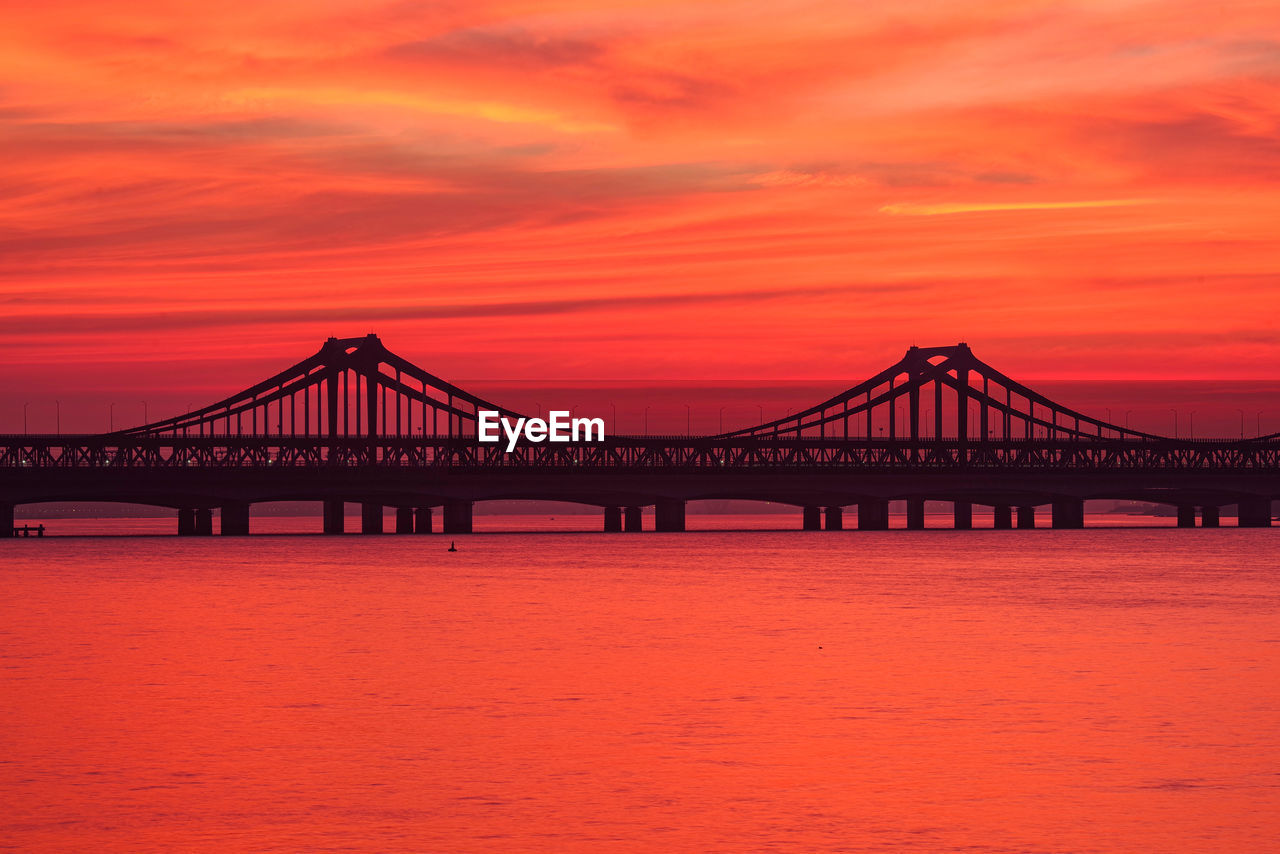 Silhouette bridge over sea against sky during sunset