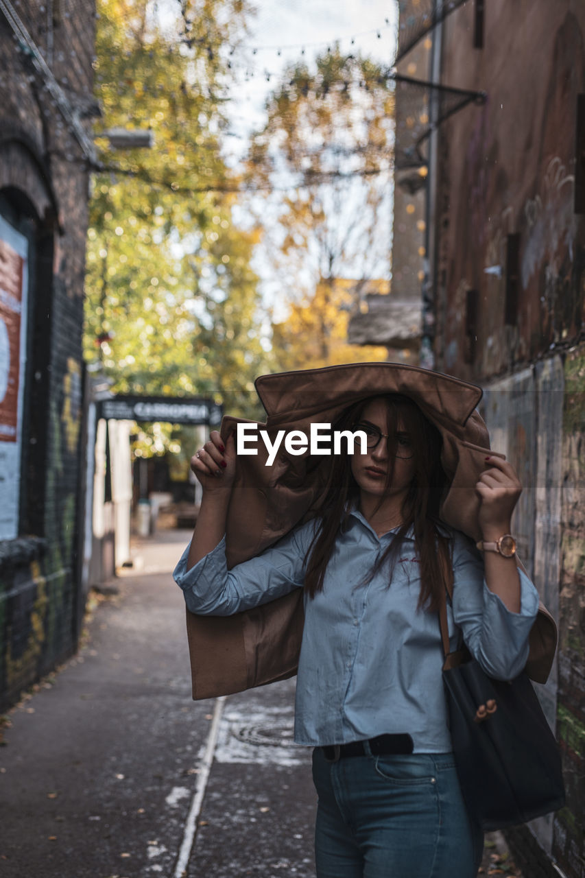 Portrait of young woman wearing jacket while standing at alley