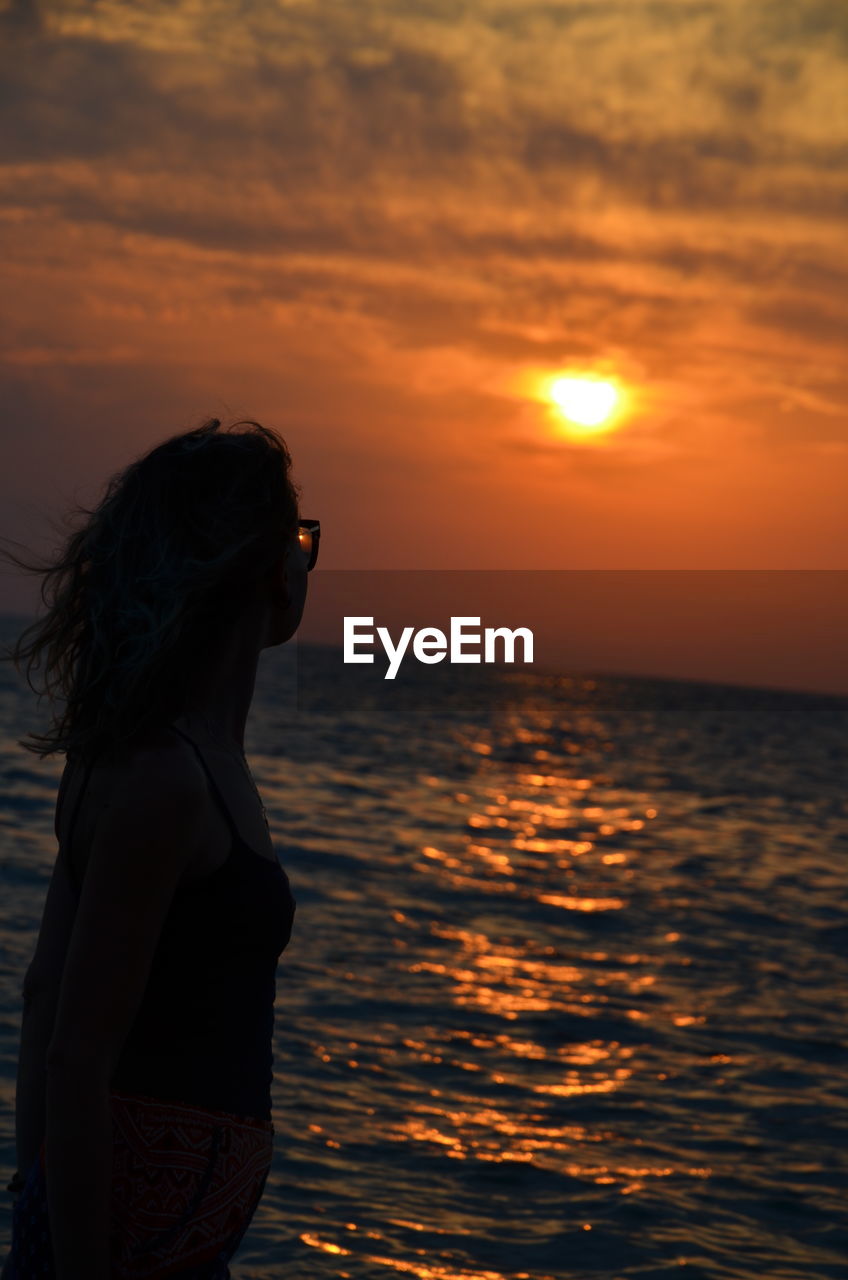 Woman standing by sea against sky during sunset