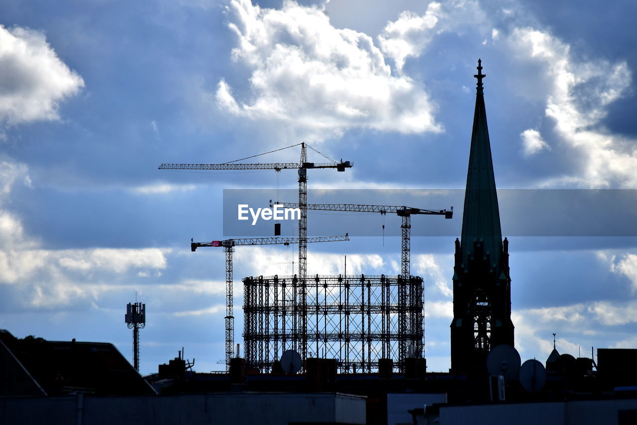 LOW ANGLE VIEW OF SILHOUETTE CRANES BY BUILDINGS AGAINST SKY