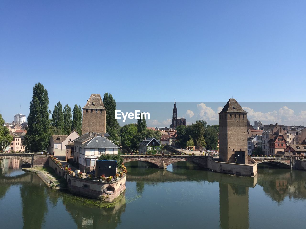 Buildings by river against clear blue sky