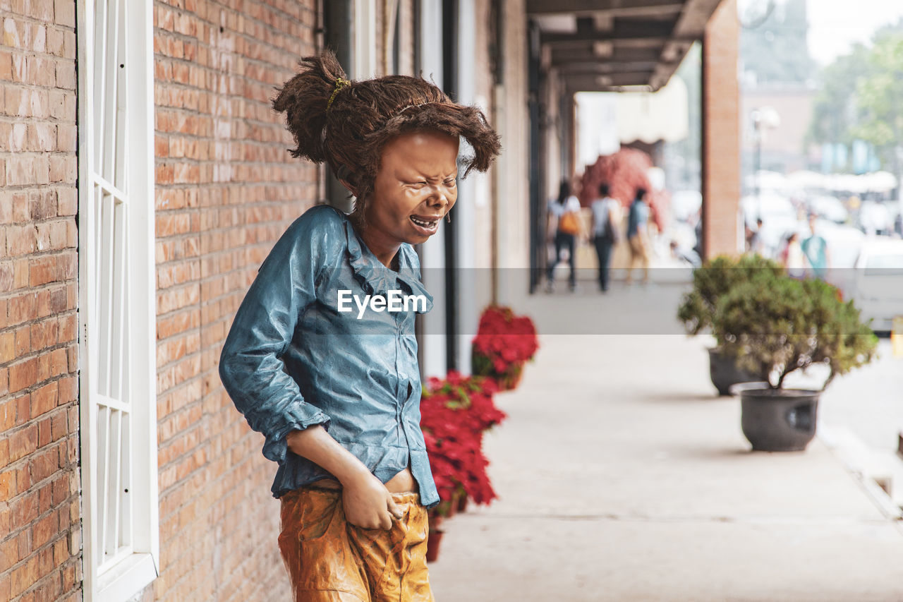 YOUNG WOMAN SMILING WHILE STANDING AGAINST BUILDING IN CITY