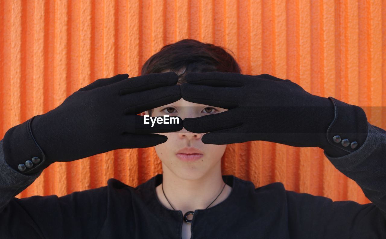 Close-up portrait of boy wearing gloves against orange wall