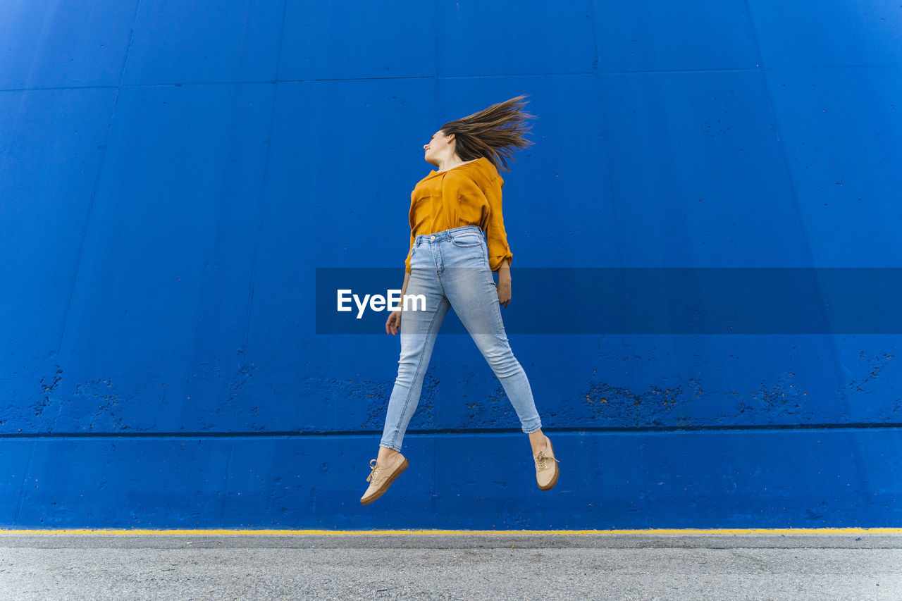 Young woman jumping in front of a blue wall