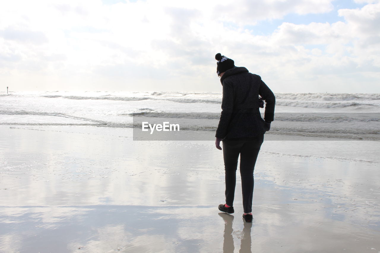 REAR VIEW OF WOMAN STANDING ON BEACH