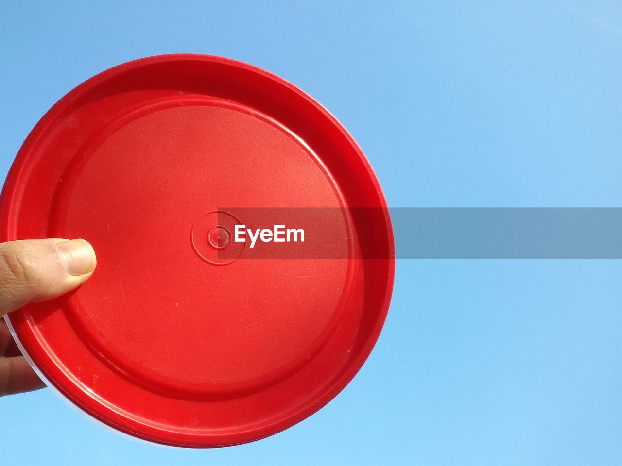 Cropped hand holding red plastic container against clear sky