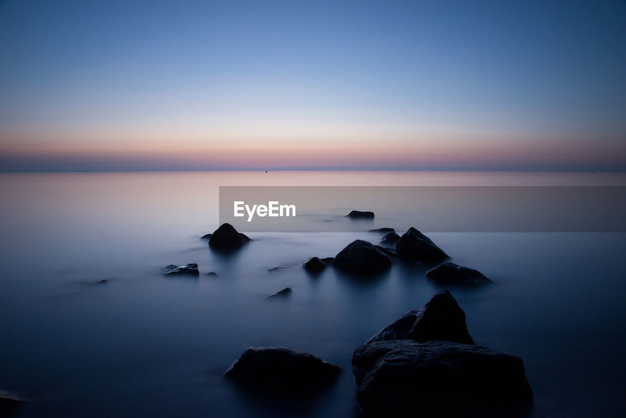 Rocks in sea against sky at sunset