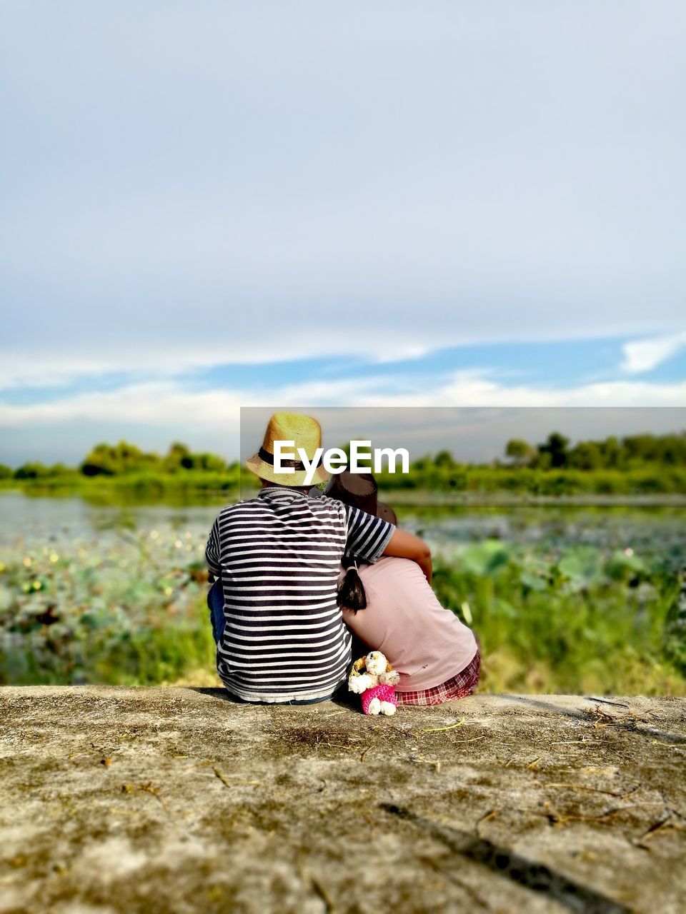 Rear view of couple sitting on rock against sky