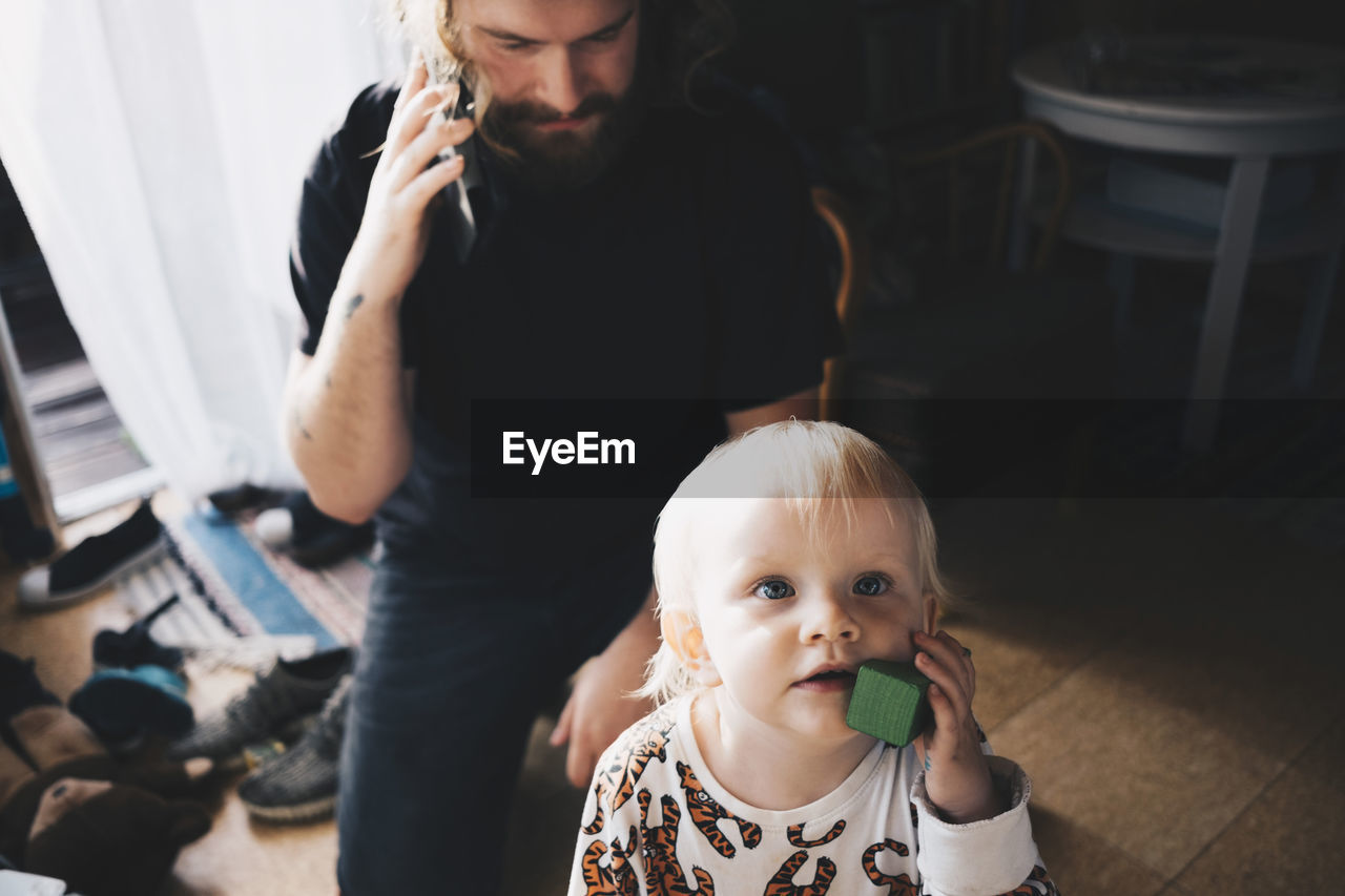 Father talking on mobile phone while girl playing with toy at home