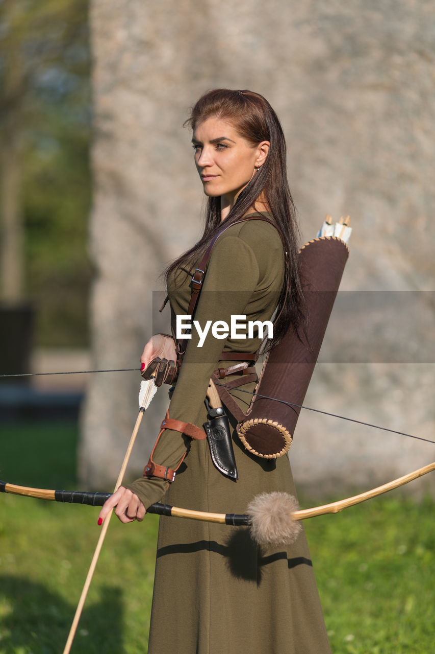 Beautiful woman holding bow and arrow standing outdoors