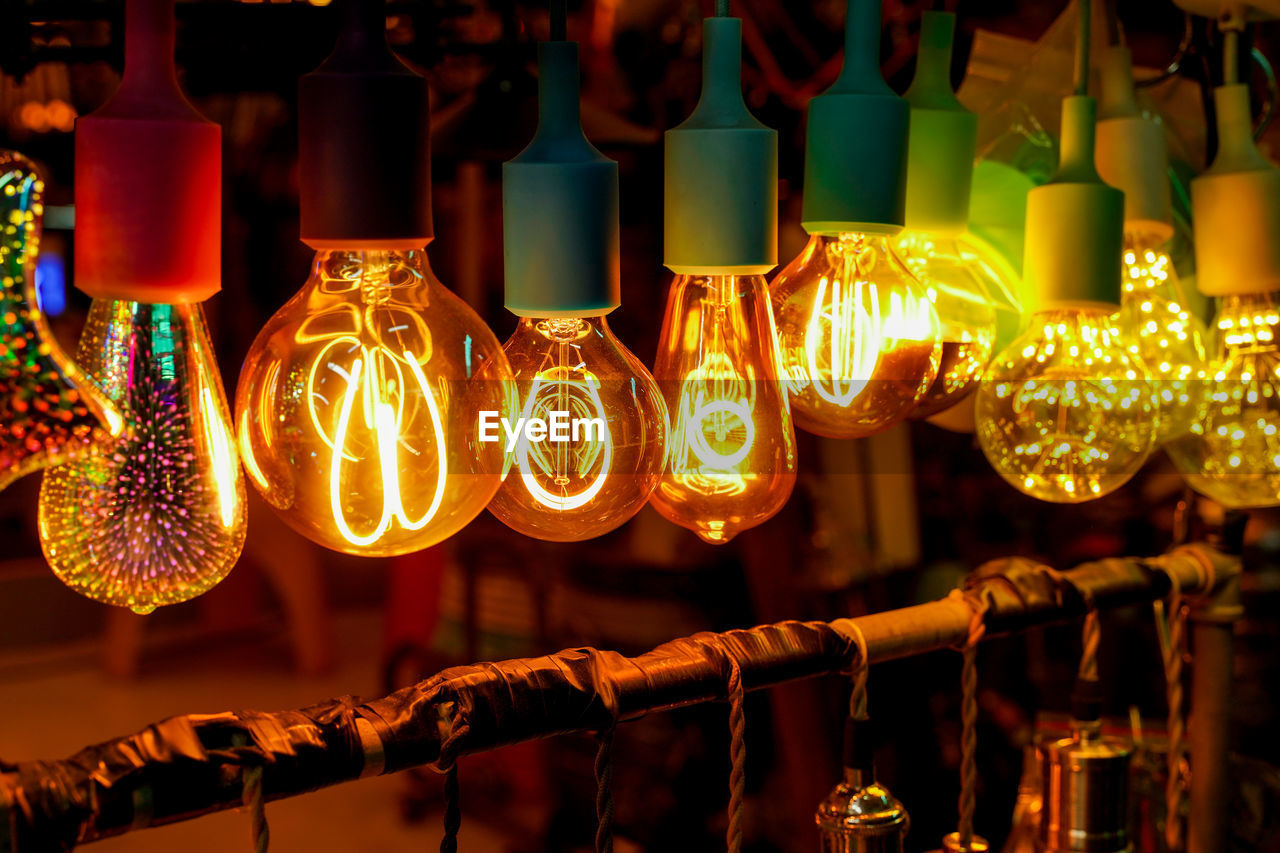 CLOSE-UP OF ILLUMINATED LIGHT BULBS HANGING IN ROW AT NIGHT