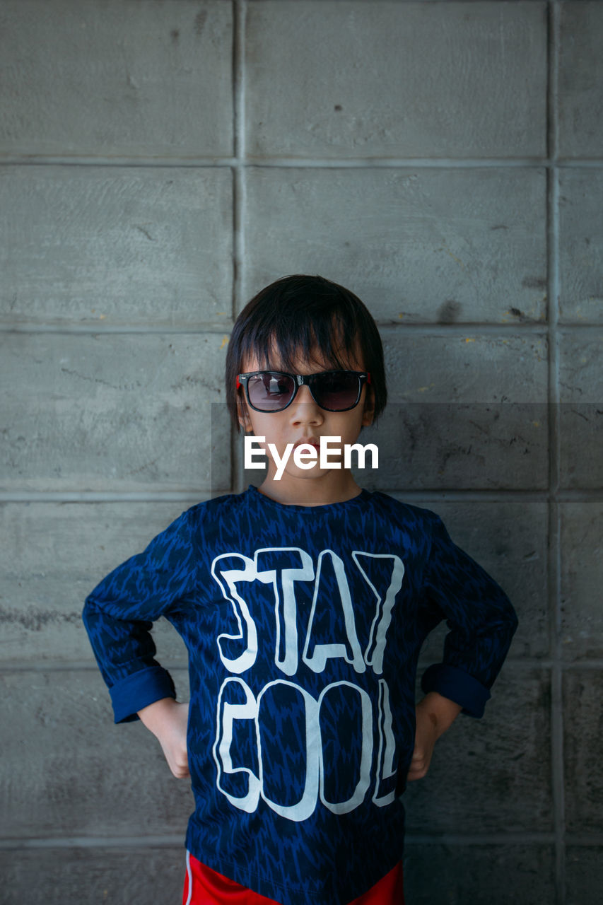 Serious boy with sunglasses against wall