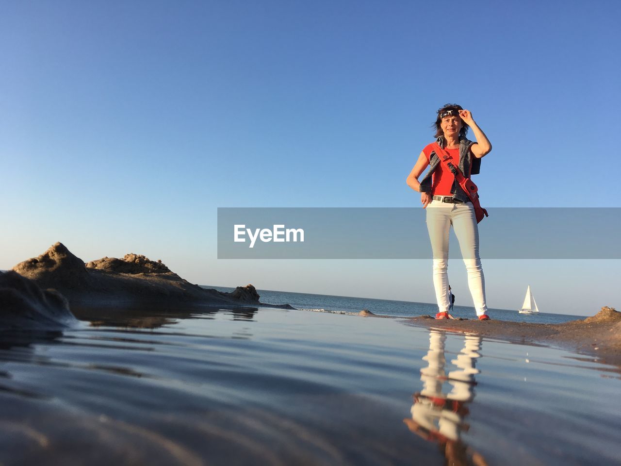 YOUNG WOMAN STANDING ON SEA AGAINST CLEAR SKY