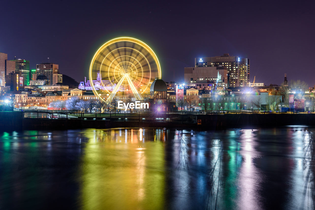ILLUMINATED FERRIS WHEEL BY RIVER AGAINST SKY AT NIGHT