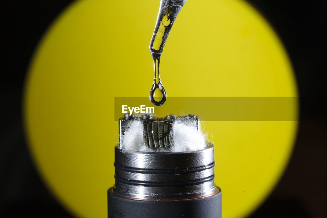 Macro shot of liquid drop on electronic cigarette against yellow background