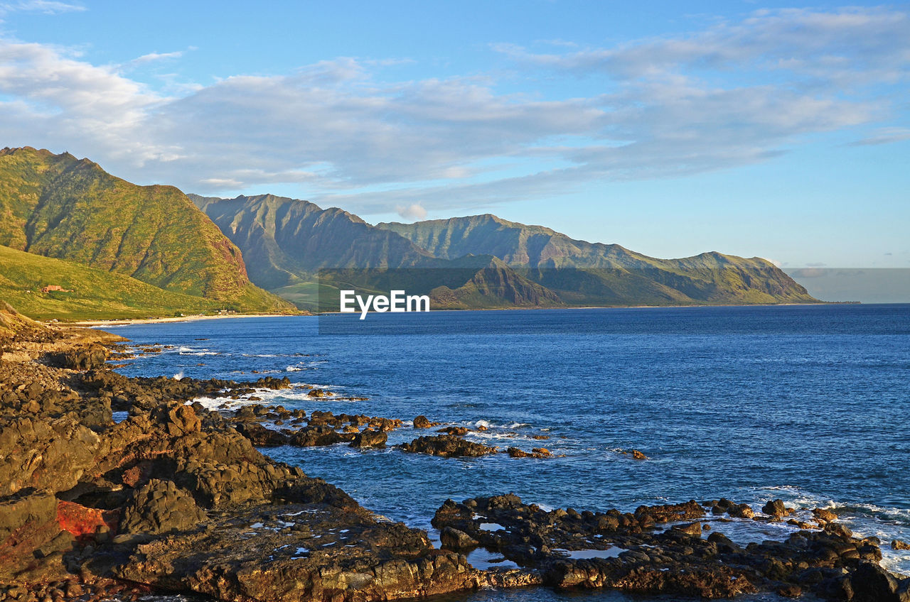 View of a calm ocean, rocky coastline and waianae mountain range at sunset on west oahu, hawaii.