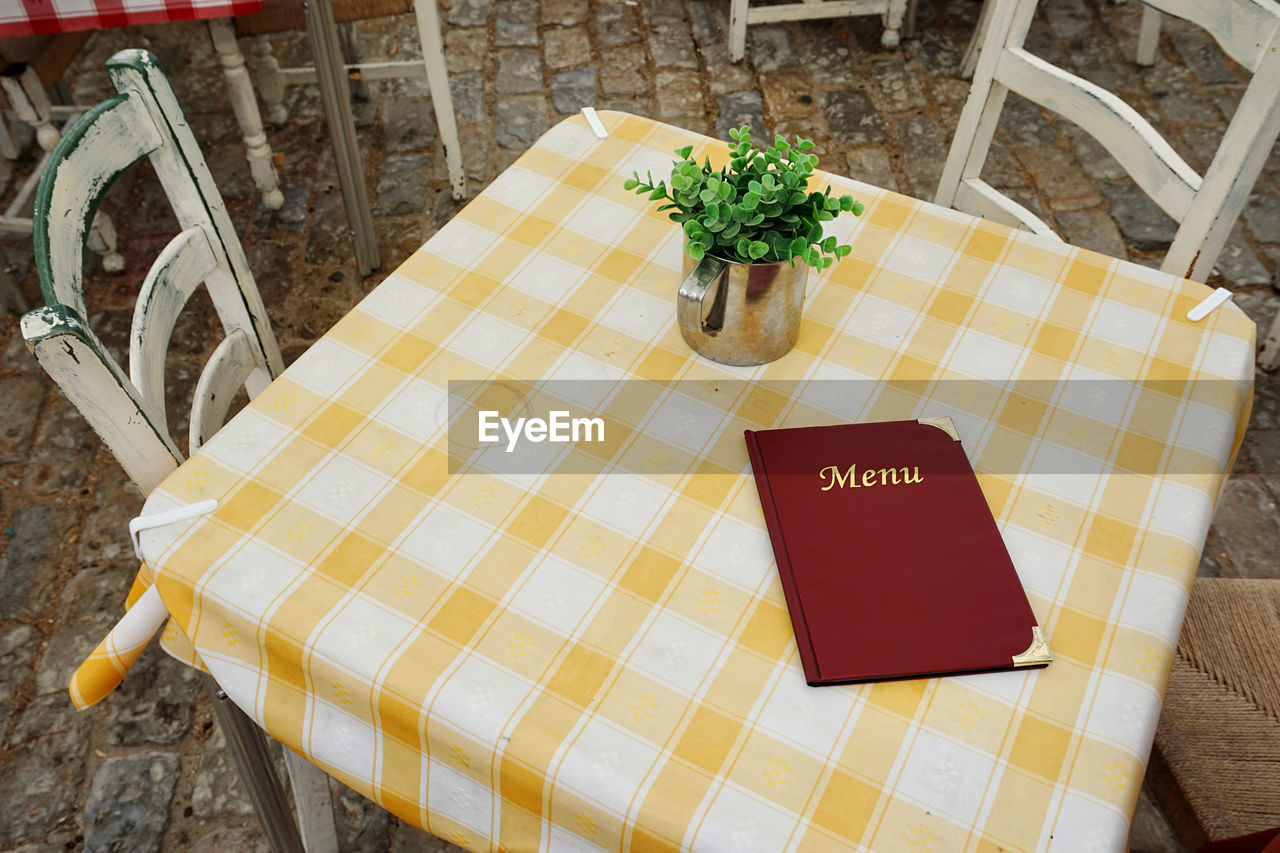 tablecloth, furniture, table, high angle view, chair, seat, no people, plant, food and drink, yellow, text, nature, flower, textile, houseplant, food, outdoors, day, communication, wood, freshness, restaurant