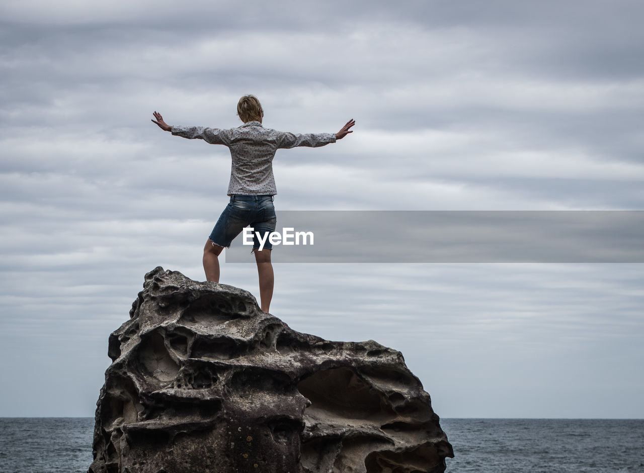 Woman standing at the coast with her arms outstretched