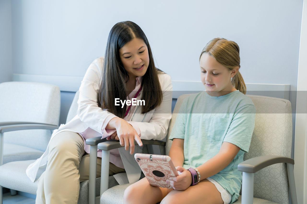 Pediatrician looking at girl using tablet computer in hospital