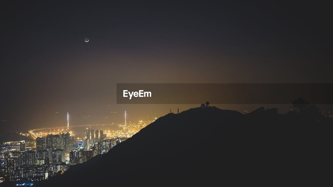 Silhouette mountain with illuminated cityscape in background at night