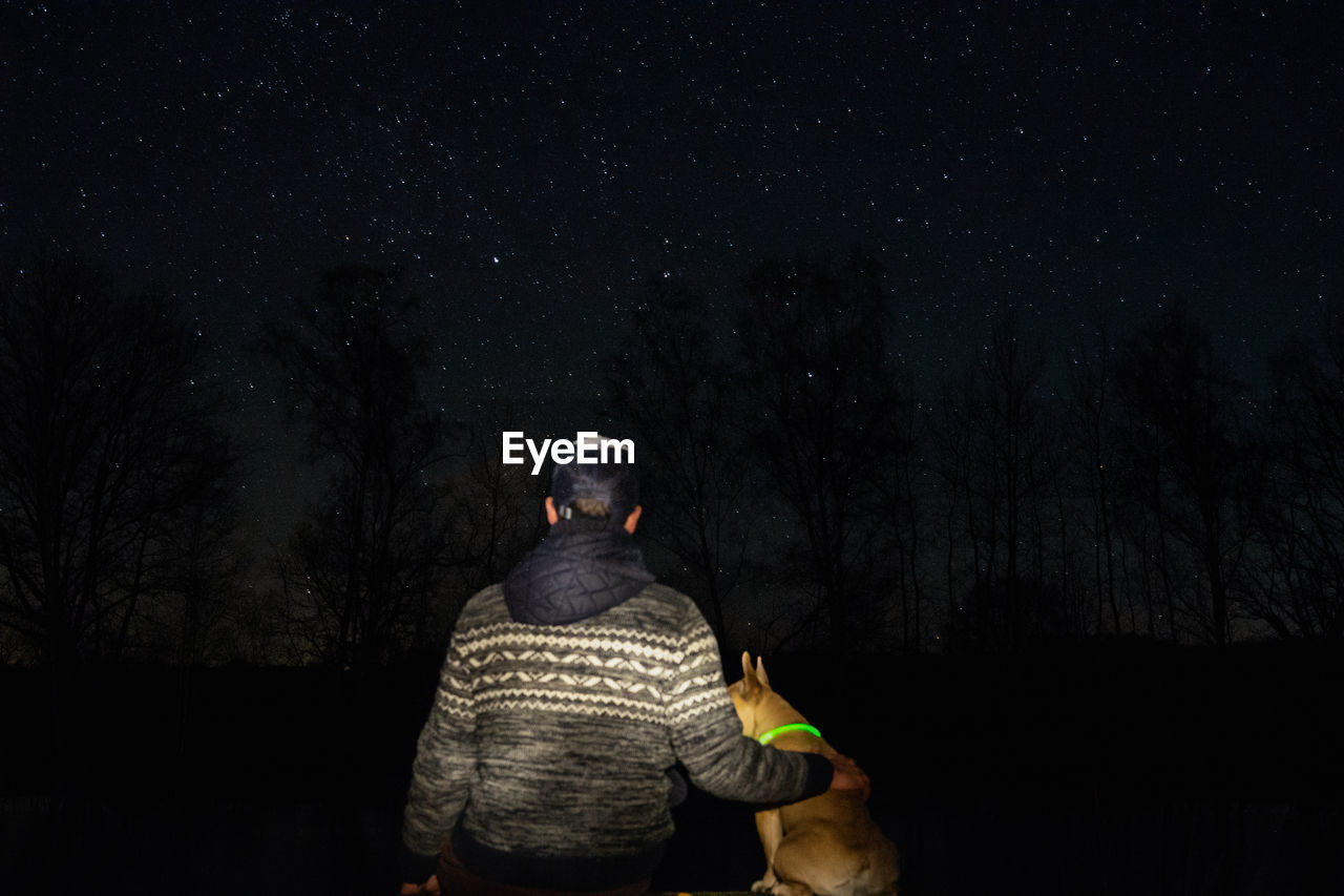 Rear view of man with dog in forest against star field at night