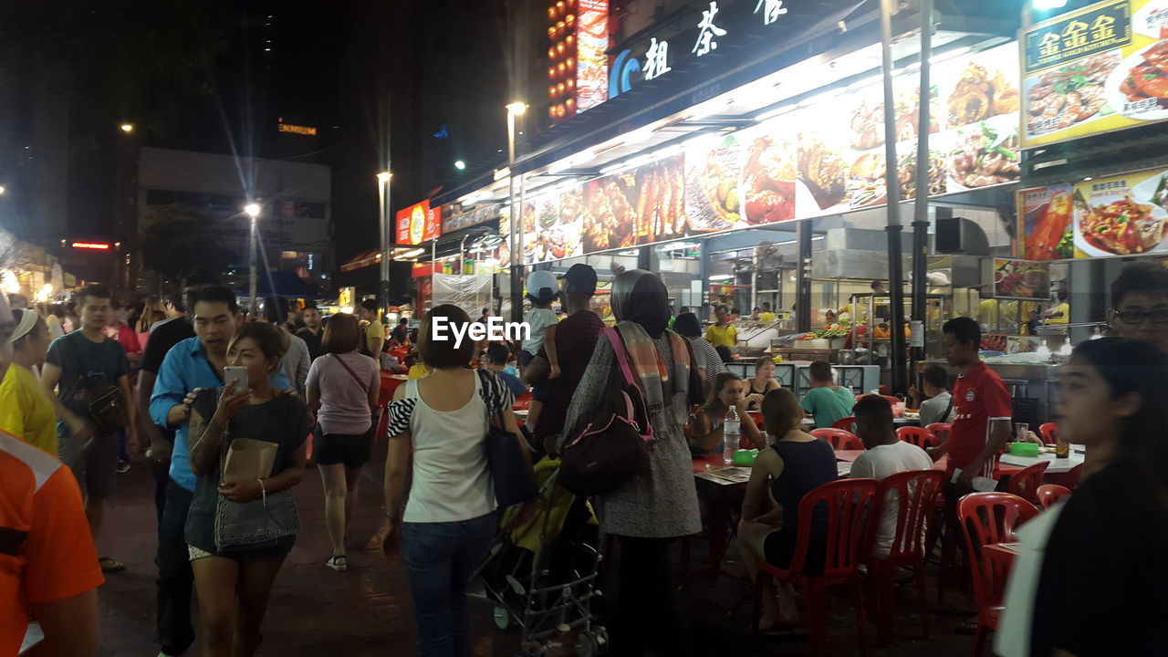 crowd, city, group of people, architecture, night, large group of people, illuminated, city life, street, building exterior, men, adult, women, food and drink, built structure, business, city street, lifestyles, market, leisure activity, road, retail, public space, bazaar, travel, travel destinations, food, communication, shopping, nightlife, outdoors, yatai, person