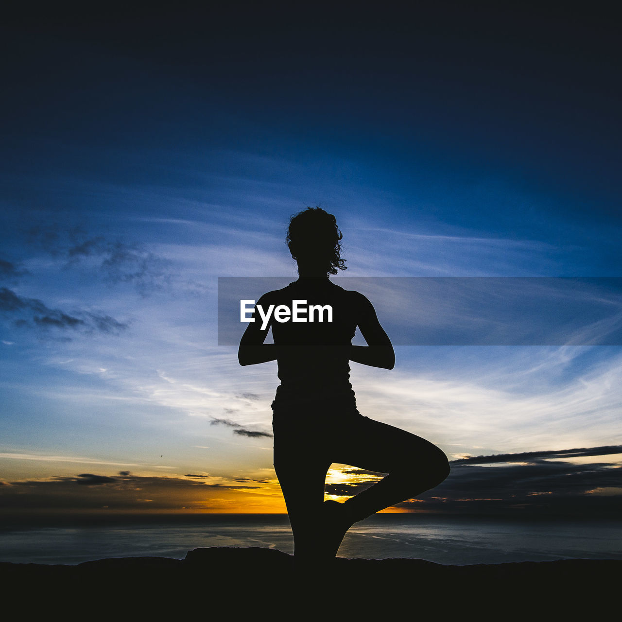 Silhouette woman practicing yoga at beach against sky during sunset