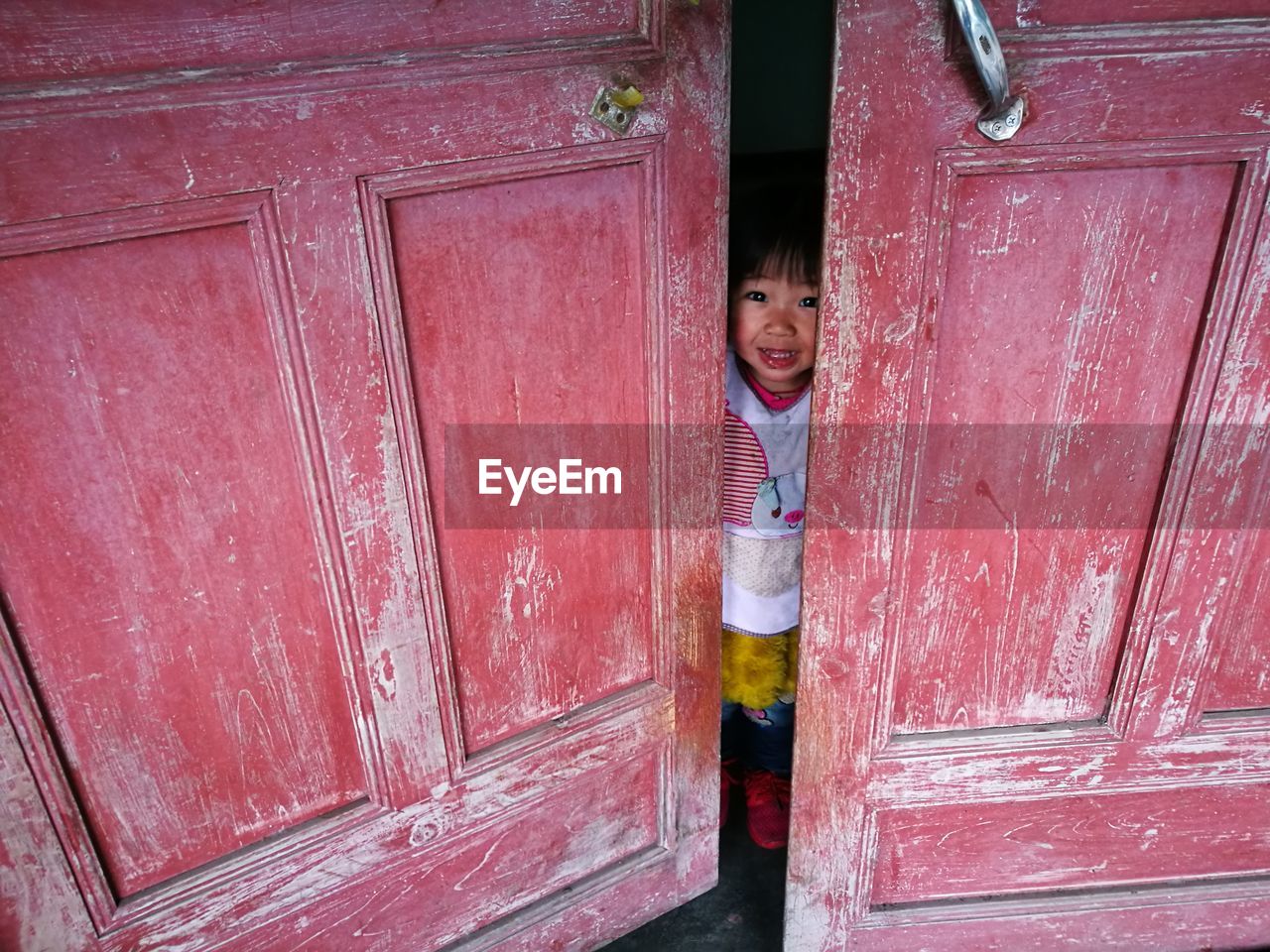 Portrait of smiling girl standing behind red door