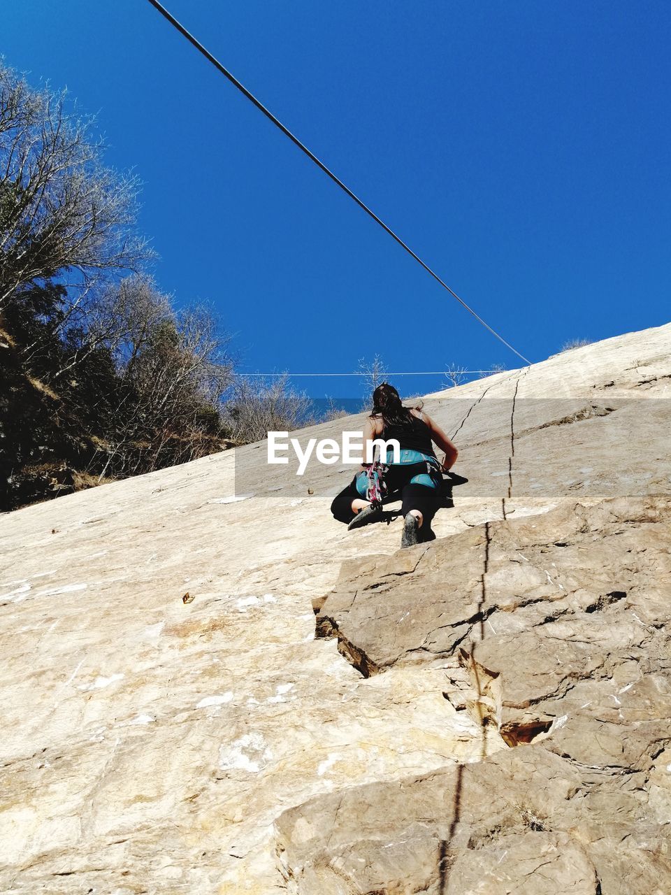 Low angle view of woman climbing wall against clear sky