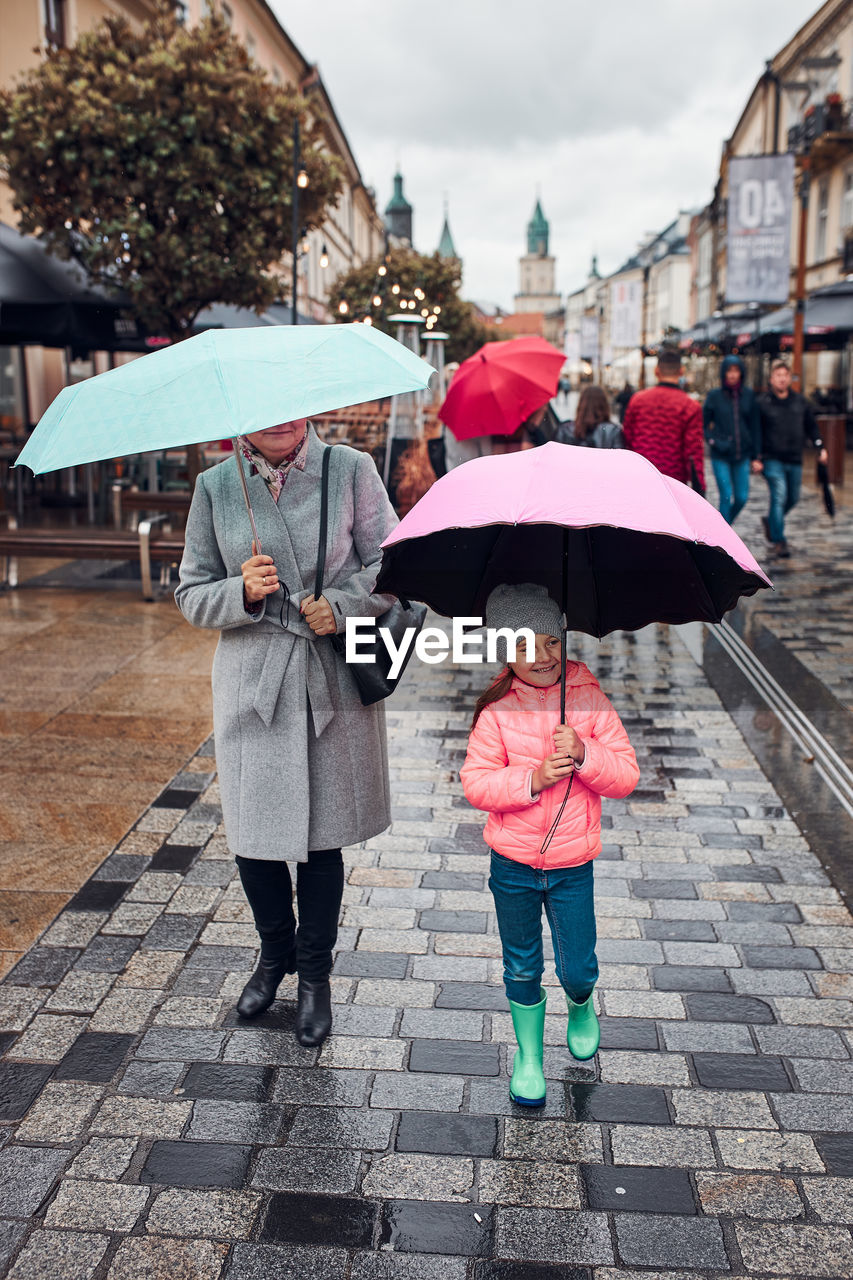 Mother and her little daughter holding the pink and blue umbrellas walking in a downtown